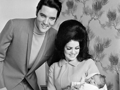 Priscilla Presley is carrying and looking at baby Lisa Marie Presley as Elvis Presley is standing next to her.